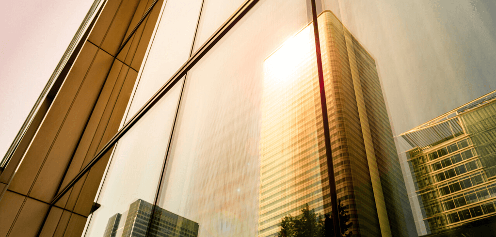 Modern glass skyscrapers with sunlight reflecting off their facades, creating a warm golden glow in an urban setting.