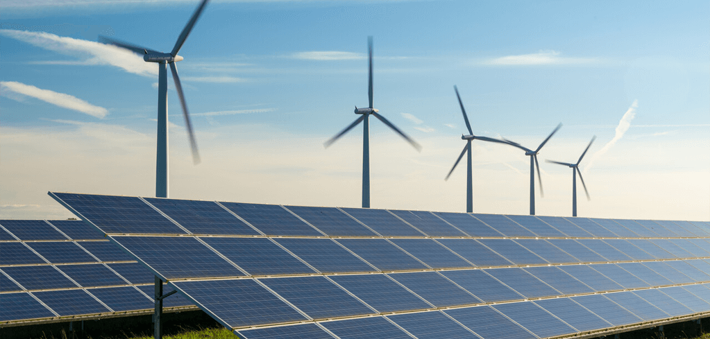 Solar panels in foreground with wind turbines behind against a blue sky, showcasing renewable energy sources.