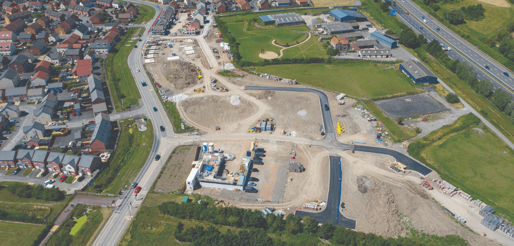 Aerial view of a construction site with new roads being developed near residential housing and a highway.