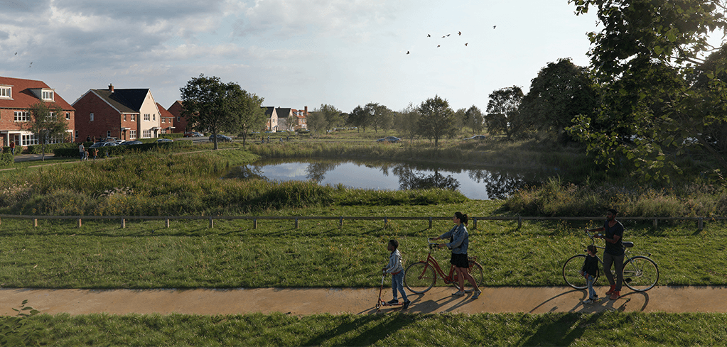 A family with bicycles walks along a path beside a green park with a pond, near a residential neighborhood.