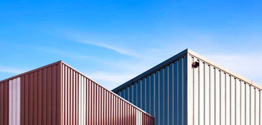 Two metal industrial crates with corrugated walls in brown and beige tones against a clear blue sky.