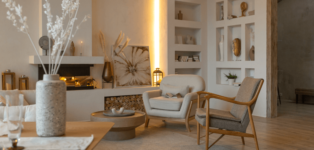 Carter Jonas LLP — Elegant neutral-toned living room with armchairs, a fireplace, built-in shelves, warm accent lighting, and decorative vases.