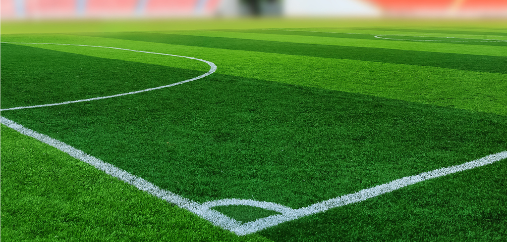Close-up of a football field corner showing bright green artificial turf with white boundary lines and curved markings.
