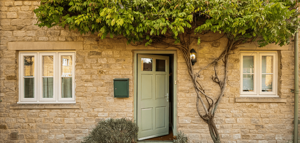 Charming stone cottage with green door, white windows, and climbing vines growing above the entrance.