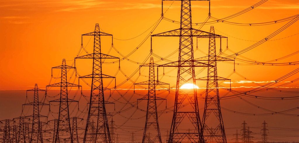 Silhouettes of electrical transmission towers and power lines against a vibrant orange sunset sky.