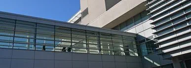 A modern institutional building exterior featuring large glass windows, metal panel cladding, and sharp architectural lines against a clear blue sky.