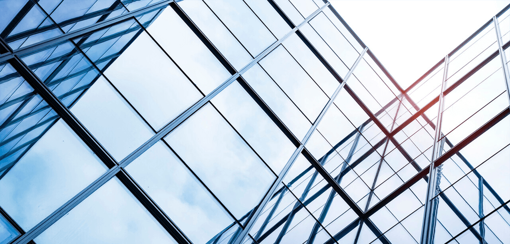 Looking up at modern glass building facade with geometric steel framework reflecting blue sky and sunlight.