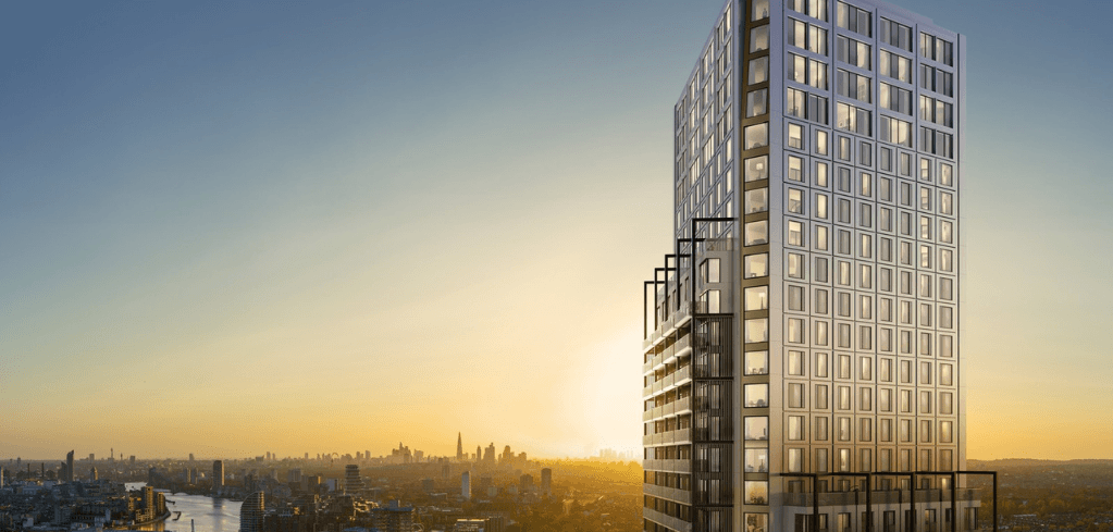 Tall modern glass skyscraper at sunset with a golden city skyline and river visible in the background.