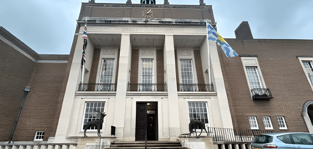 Historic brick building with white columns, clock tower, and animal statues flanking the entrance, with flags displayed.