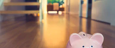This image features a pink piggy bank placed on a polished wooden floor, symbolizing savings, investment, and financial planning within a home setting. The softly blurred background of a bright, modern interior adds a warm and inviting feel, reinforcing themes of property investment, long‑term wealth building, and smart buy‑to‑let strategies