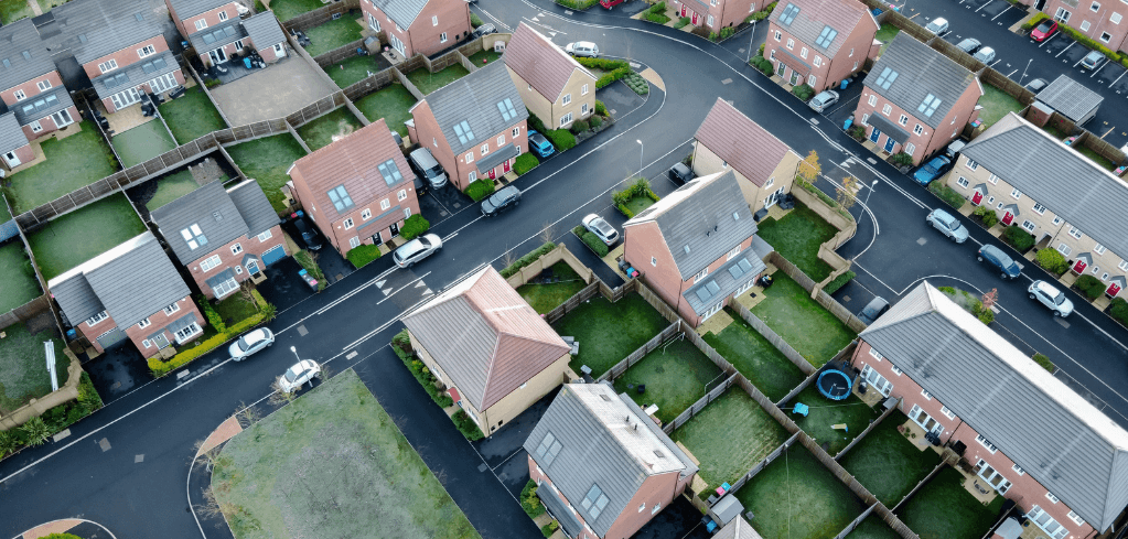 Aerial view of a residential neighborhood with brick houses, green yards, parked cars, and winding roads.