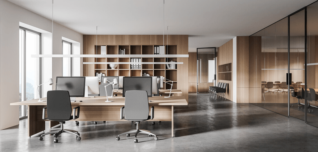 Modern office space with wooden desks, gray chairs, computer monitors, wooden shelving, and glass-walled meeting room.