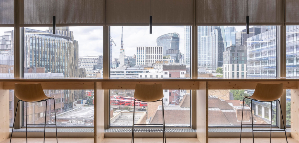 Three brown barstools facing large windows with panoramic view of London skyline featuring the Walkie-Talkie building and skyscrapers.