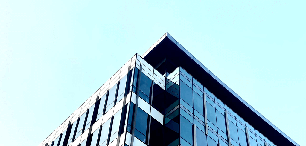 Modern glass office building corner with sleek geometric design against light blue sky.