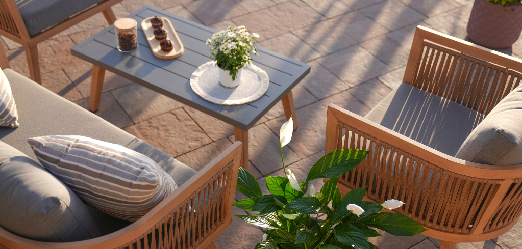 Overhead view of a sunny patio with wooden furniture, gray cushions, a coffee table with flowers, and a green plant nearby.