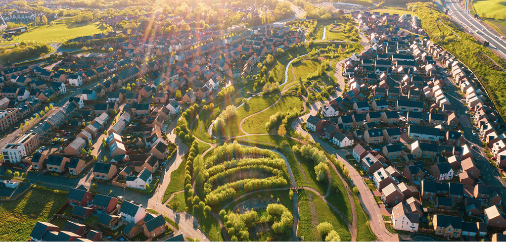 Aerial view of suburban housing development with winding green park space and walking paths at sunset, golden light illuminating the landscape.