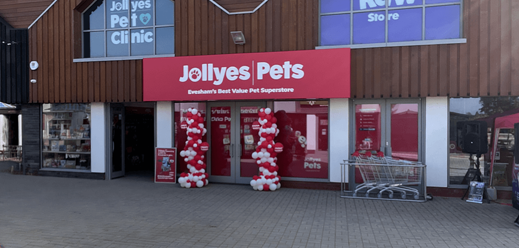 Exterior of Jollyes Pets store in Evesham with red signage, red and white balloon columns flanking the entrance, and shopping carts outside.