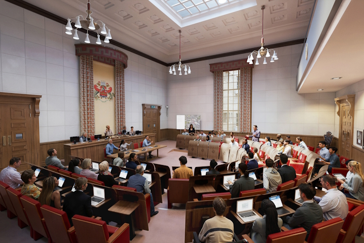 A formal lecture hall with red seats, students using laptops, and a presenter at the front beneath a skylit ornate ceiling.