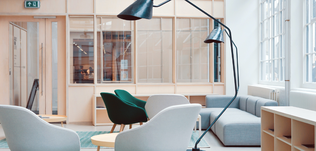 Modern office lounge with green and white chairs, light blue sofa, black floor lamp, and glass partition walls.