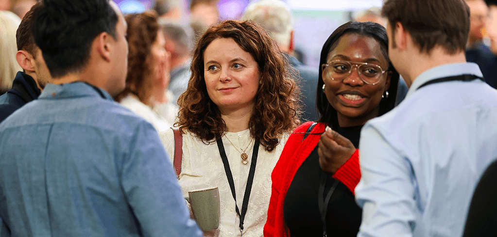 Diverse group of professionals networking at a conference, wearing lanyards and engaged in conversation.