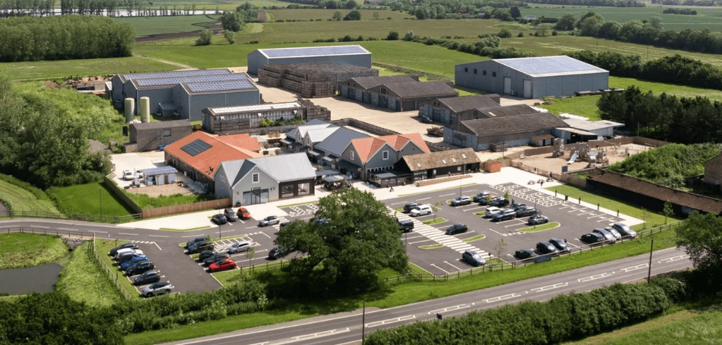 Aerial view of a rural farm complex with solar-paneled warehouses, retail buildings, parking lots, and surrounding green fields.