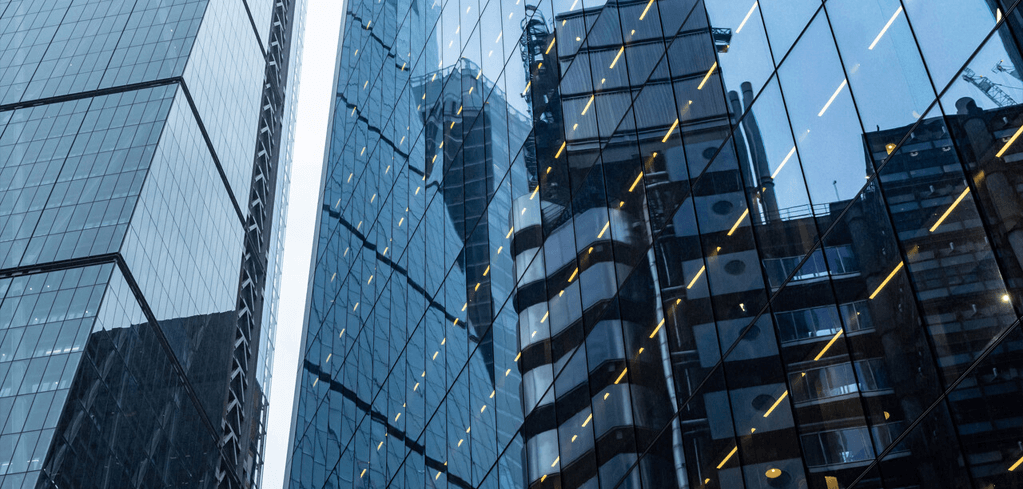Modern glass skyscrapers with blue reflective facades and geometric patterns viewed from below against a blue sky.