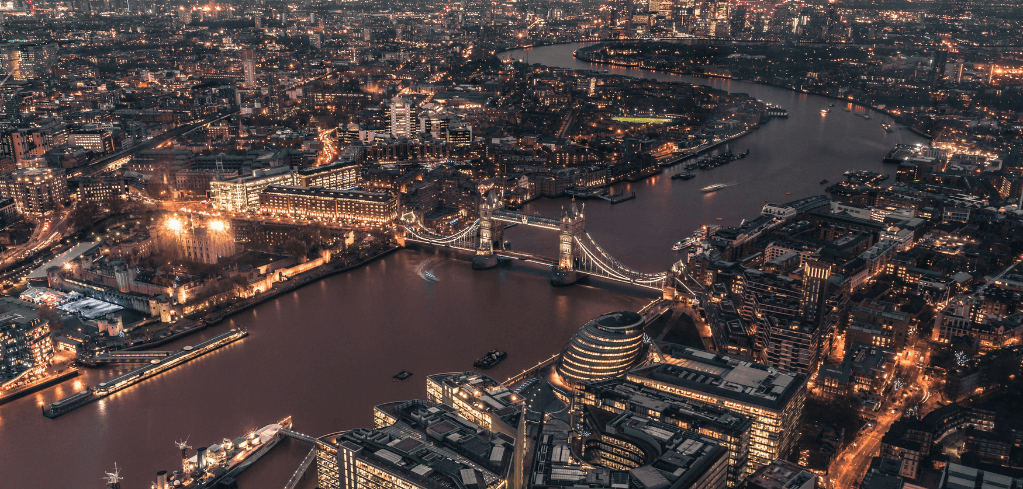 Aerial night view of London with Tower Bridge spanning the River Thames, city lights illuminating the skyline.
