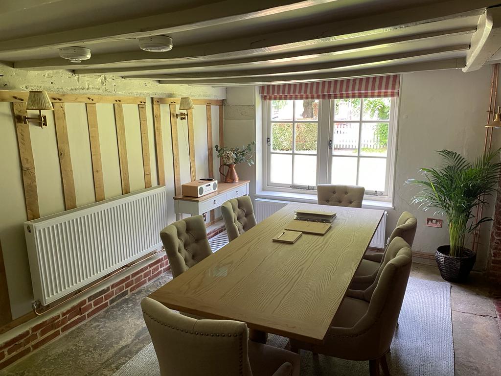 Cozy dining room with wooden table, beige chairs, exposed beams, striped window treatment, and potted plant by window.