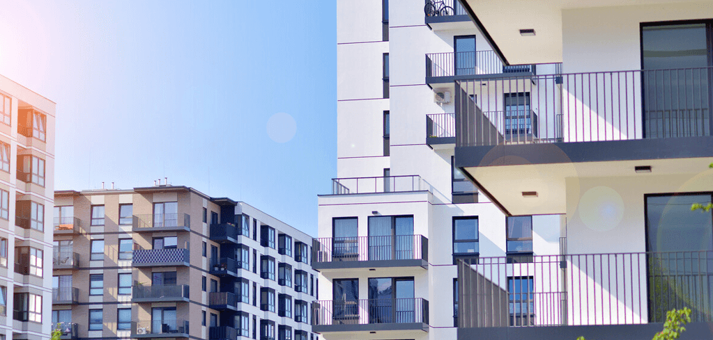 Modern apartment buildings with balconies against a clear blue sky, featuring white and neutral-colored facades.