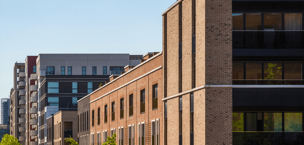 Modern brick apartment buildings with glass balconies against a clear blue sky in an urban residential development.
