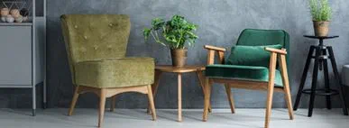 This image showcases a beautifully styled modern living room with mid‑century green armchairs, a solid wooden side table, and lush indoor plants. Set against a grey textured wall, the space blends natural materials with contemporary interior décor trends. 