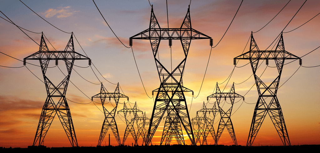 Silhouettes of electrical transmission towers against a vibrant orange and pink sunset sky, power lines stretching between them.