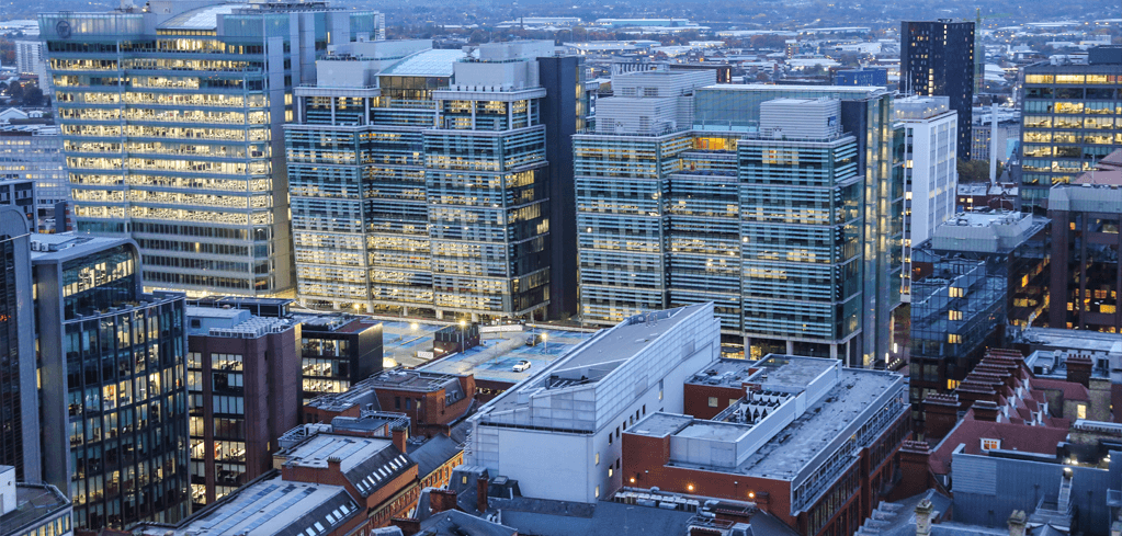 Aerial view of illuminated modern office buildings and skyscrapers in a city skyline at dusk.