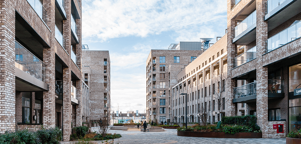 Modern brick apartment complex with glass balconies surrounding a landscaped courtyard under a partly cloudy sky.