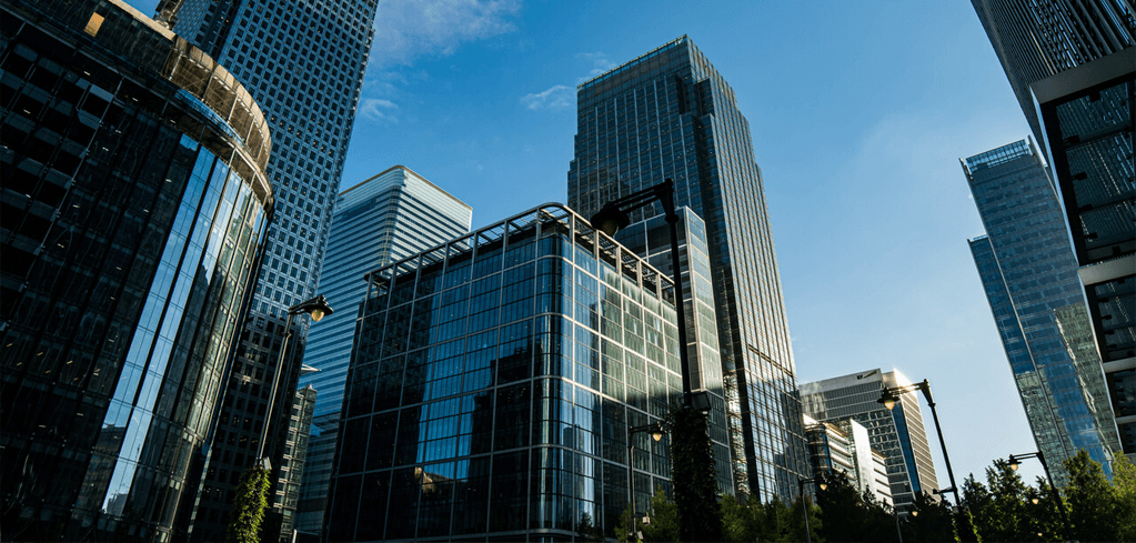 Carter Jonas LLP — Modern glass skyscrapers in a financial district with blue sky above and trees visible at the bottom of the frame.