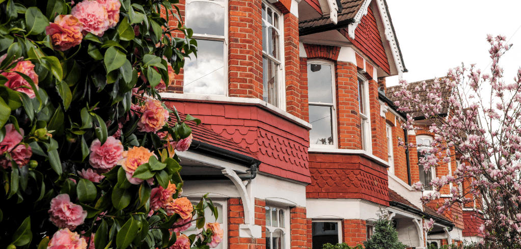 Traditional red brick house with bay windows, framed by pink flowering plants and magnolia blossoms in spring.