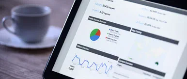 This image shows a close-up view of a tablet displaying digital analytics dashboards, including charts, graphs, and performance metrics. With a blurred coffee cup in the background, the scene highlights modern digital reporting, data-driven decision-making, and professional marketing insights.