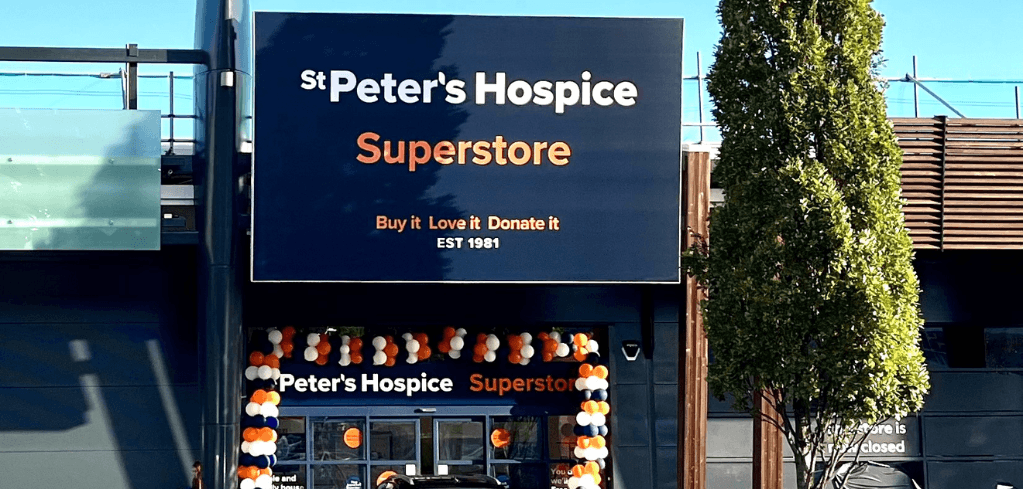 Exterior of St Peter's Hospice Superstore with orange, white, and navy balloons decorating the entrance on a sunny day.