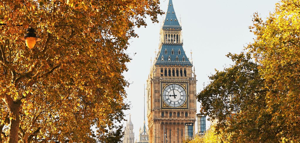 Big Ben clock tower framed by golden autumn trees in London, with a street lamp visible on the left side.
