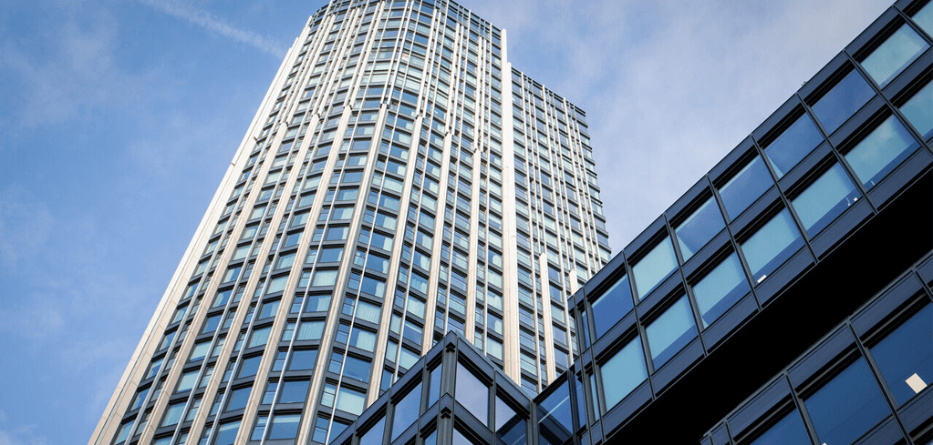 Modern glass skyscraper with white facade rising against blue sky, adjacent to a dark glass office building.