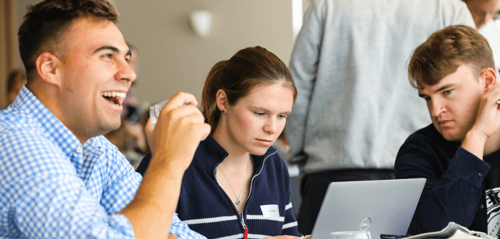Three young people in a study group, one laughing while two others focus intently on a laptop.