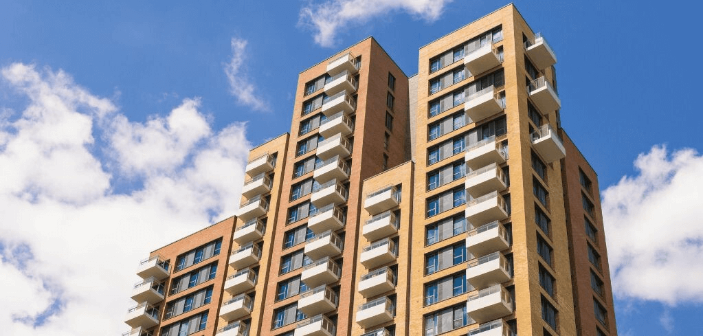 Modern brick apartment building with white balconies against a blue sky with scattered clouds.