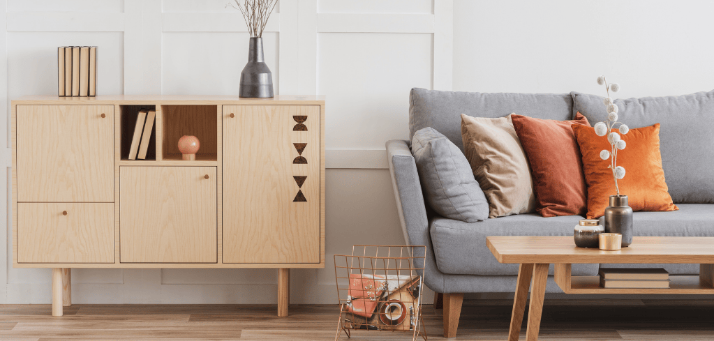 Modern living room with wooden cabinet, gray sofa with orange pillows, and wooden coffee table in minimalist style.