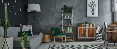 A stylish retro-inspired living room featuring a grey sofa, mid-century armchairs, and a mix of indoor plants. Textured dark walls, patterned cushions and a bold geometric rug add character, while wooden furniture and soft lighting create a warm, modern yet relaxed interior atmosphere.