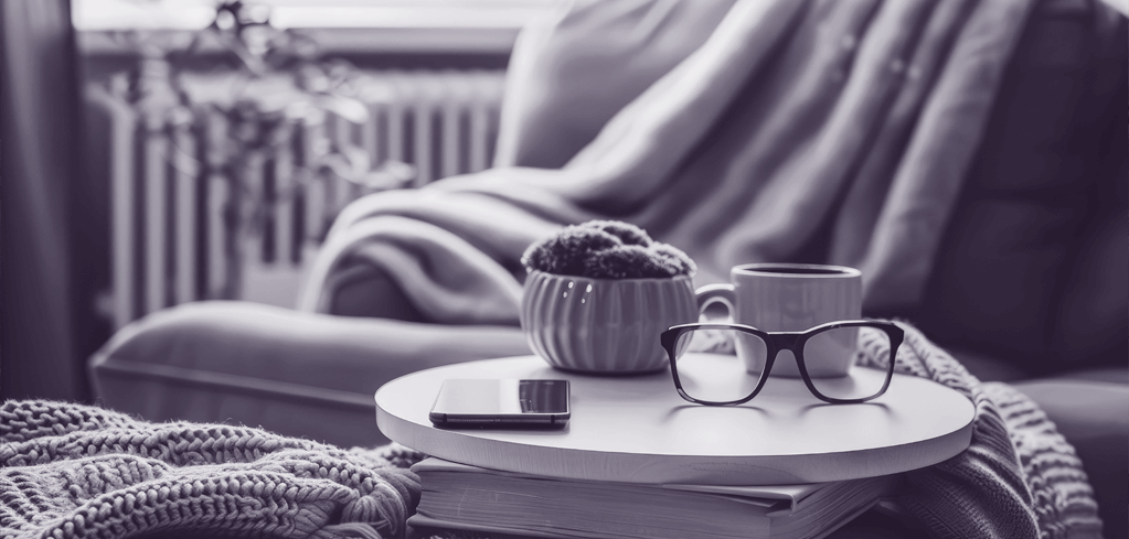 Cozy reading nook with armchair, coffee table holding eyeglasses, smartphone and mug in black and white.