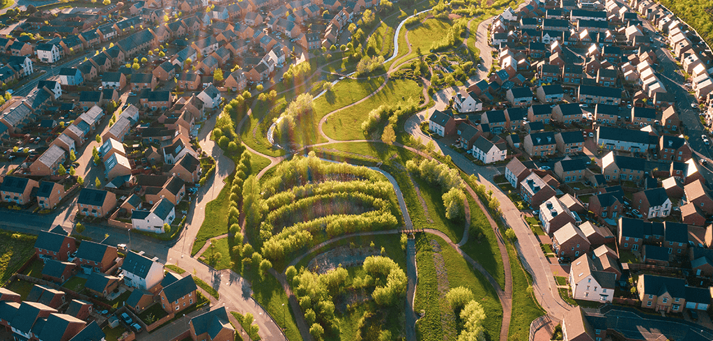 Carter Jonas LLP — Aerial view of a residential neighborhood with brick homes surrounding a lush green park with winding paths and trees.