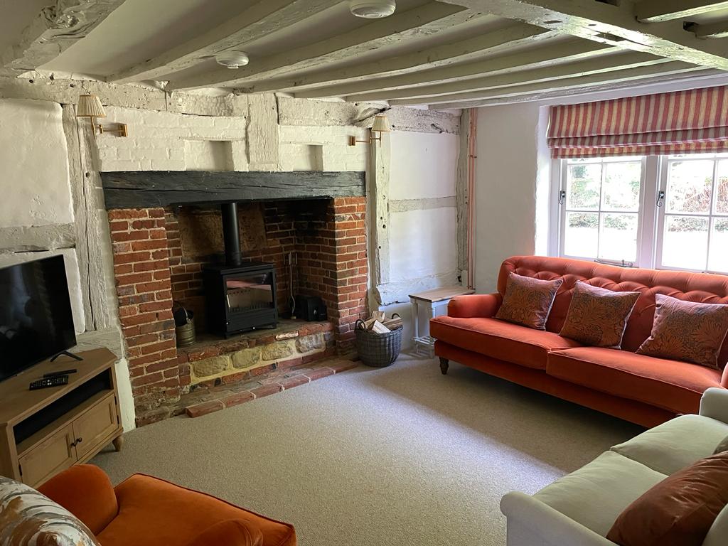 Cozy cottage living room with brick fireplace, orange sofa, exposed beams, and striped window treatments.
