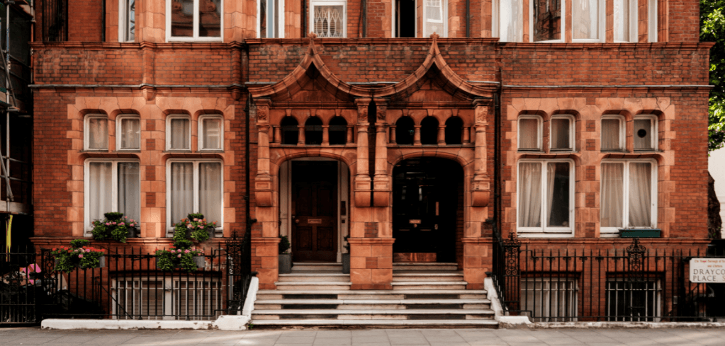 Historic red brick townhouse with ornate Gothic-style entrances, large windows with white curtains, and black iron fencing.