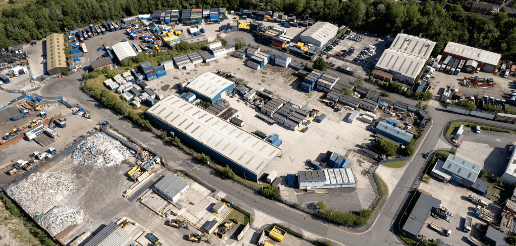Aerial view of a large industrial waste and recycling facility with warehouses, storage containers, and a debris pile.