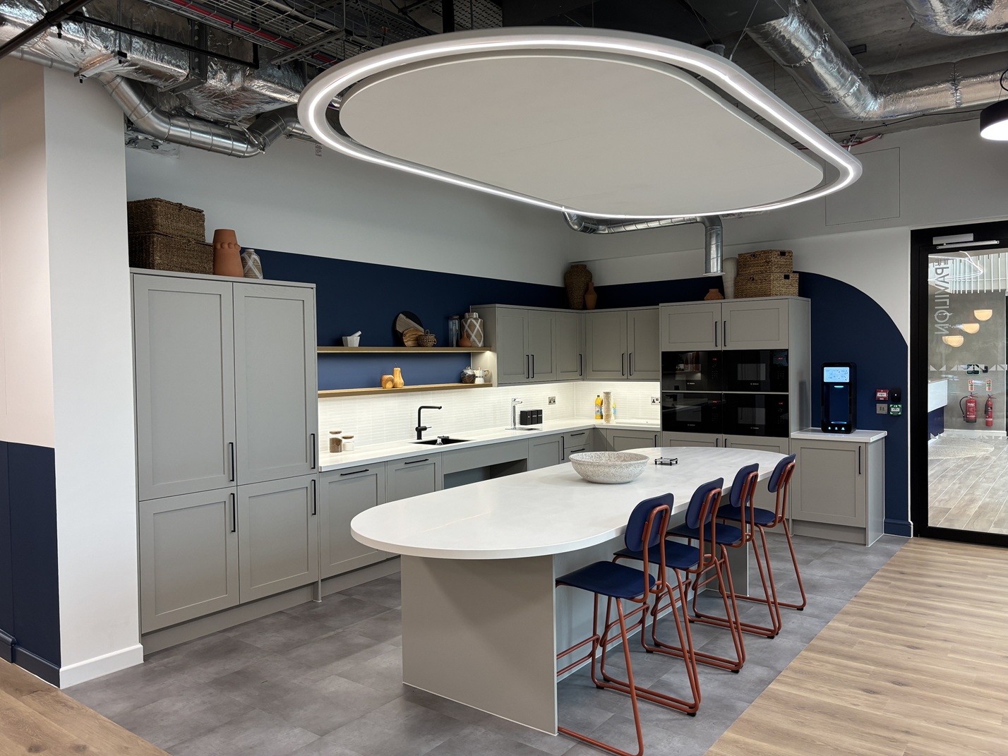Modern kitchen with gray cabinets, navy blue walls, white island with blue chairs, and distinctive oval ceiling light.
